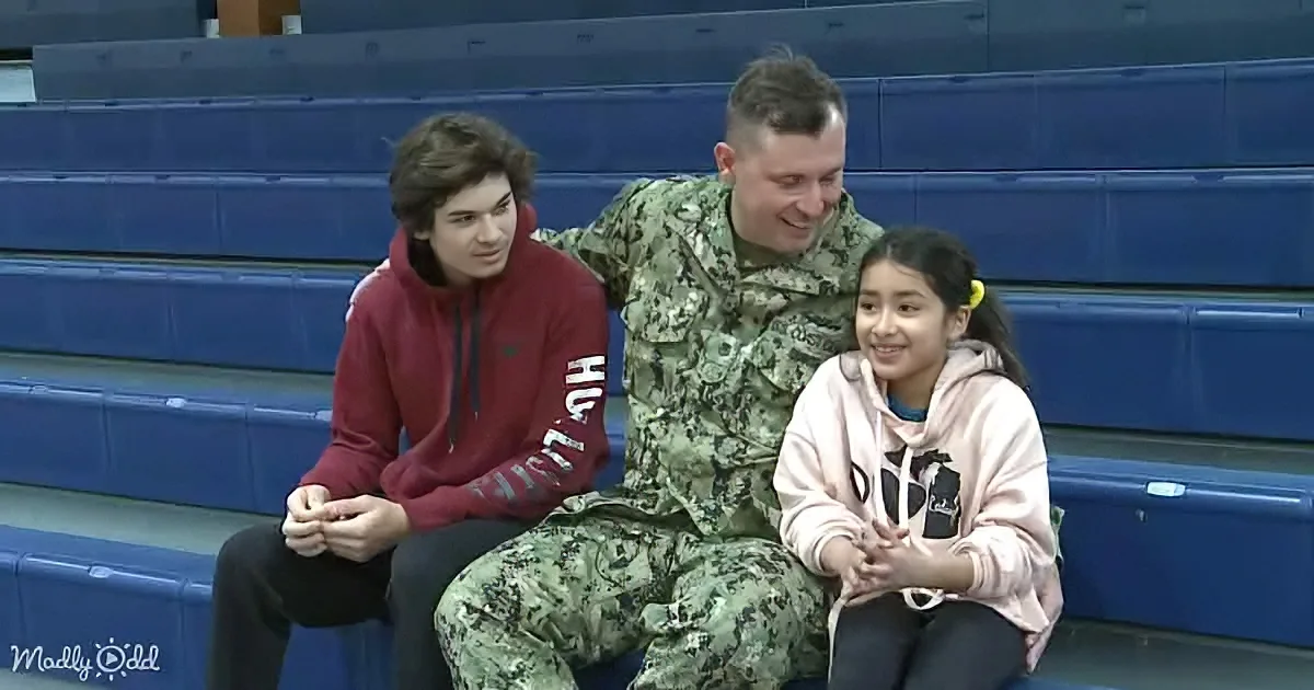 A man in military uniform sits between two children on bleachers, smiling.