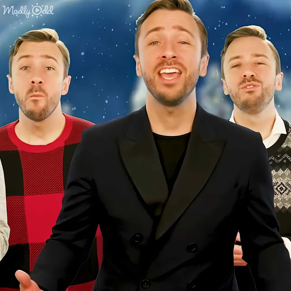 A man in a black suit is smiling, flanked by two others in festive sweaters against a snowy backdrop.