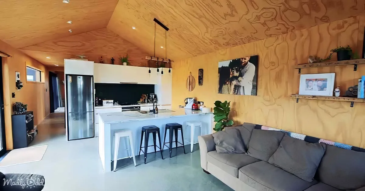A cozy living room with a wooden ceiling, a grey couch, a kitchen island, and a large painting of a man and child on the...