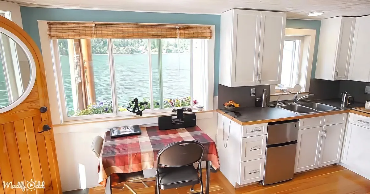 A cozy kitchen with white cabinets, a red plaid tablecloth, and a view of a lake through a large window.