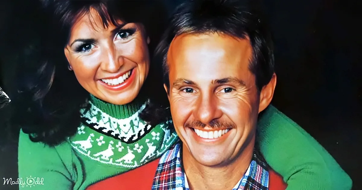 A smiling couple in festive sweaters, the woman wearing a green sweater with reindeer, the man in a plaid shirt and green...