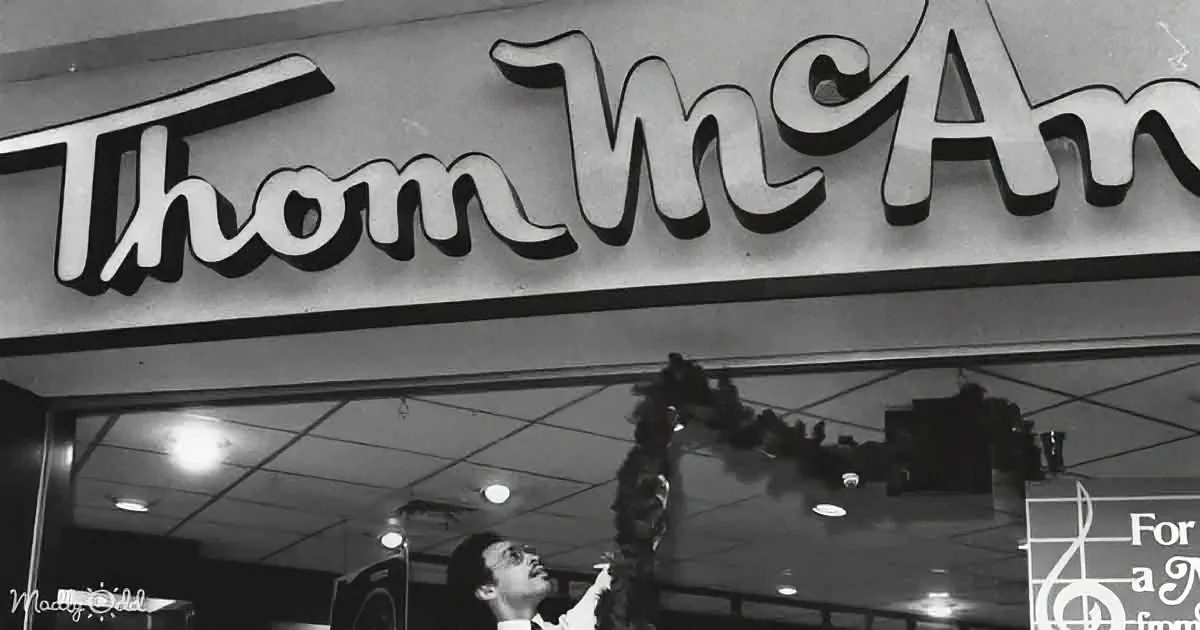 A man hangs a Christmas wreath under a "Thom McAn" sign in a store.