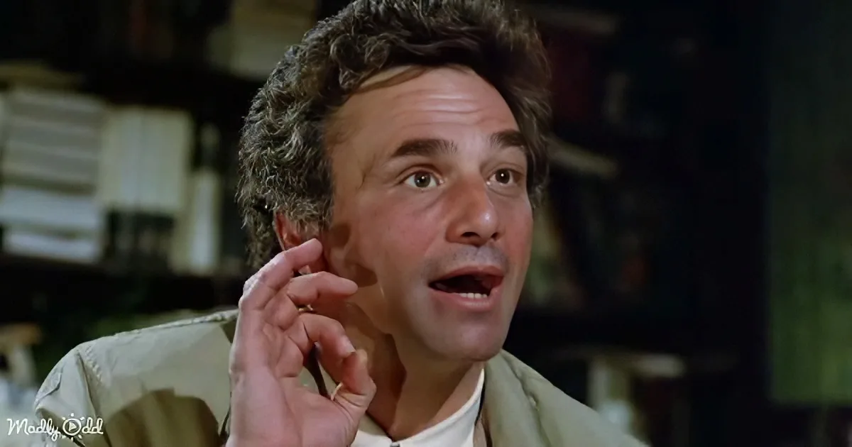 A man with curly hair, wearing a light jacket, holds his hand to his ear, appearing surprised or concerned.