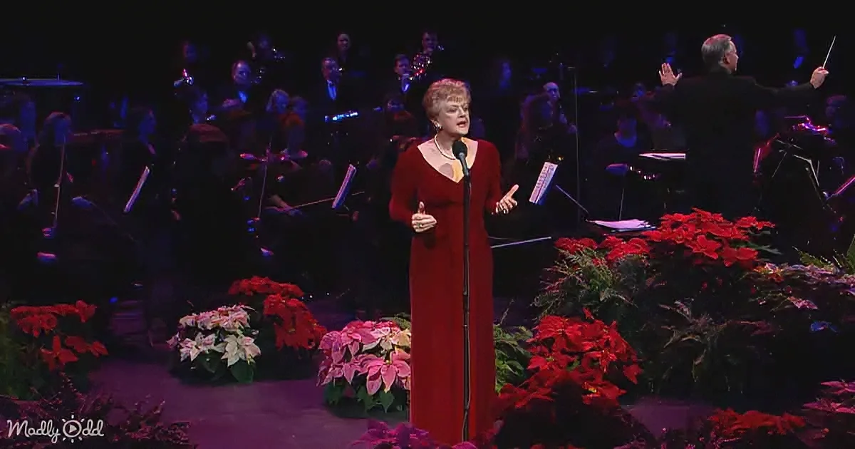 A woman in a red dress sings into a microphone, surrounded by poinsettias and an orchestra.