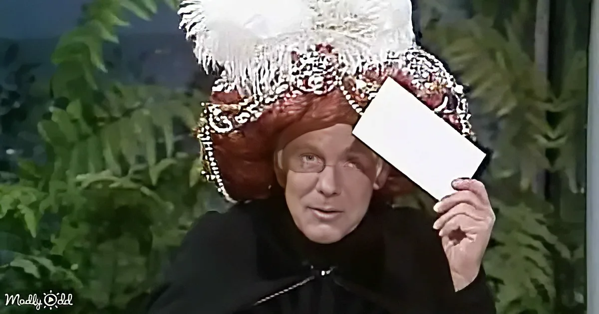 A person in a black outfit and ornate hat holds a white card in front of their face.