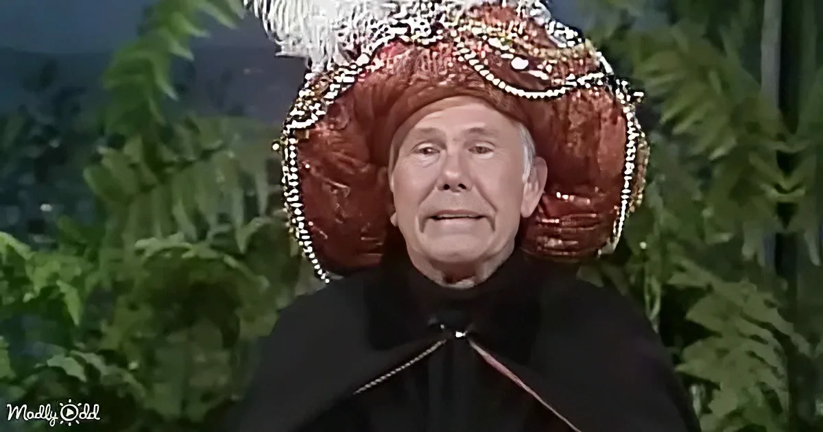 A person in a black outfit wears an elaborate red headdress with feathers and beads, set against a backdrop of green foliage.