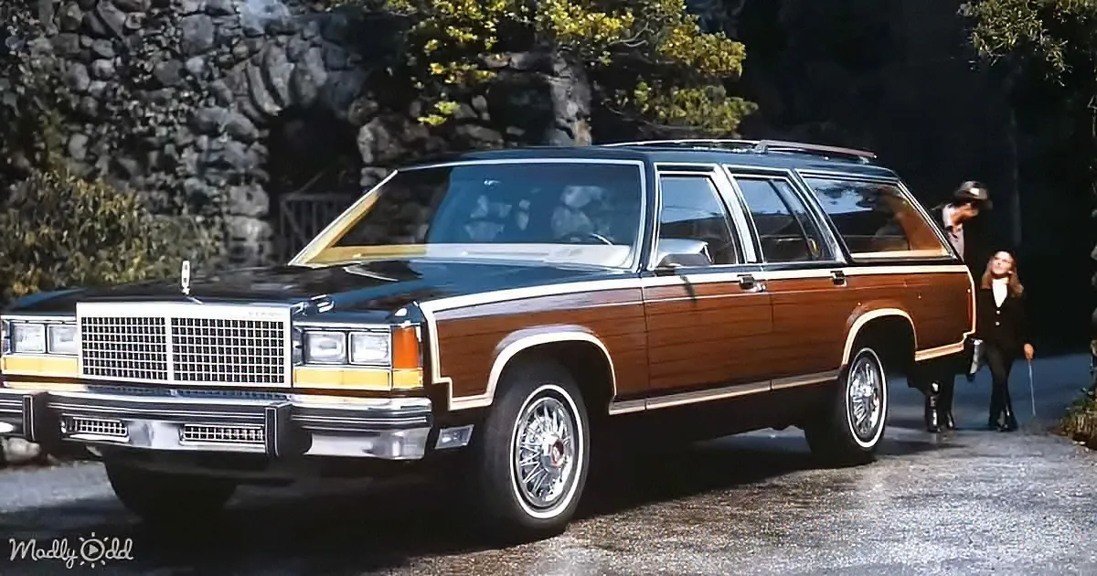 A classic wood-paneled station wagon with a black roof and chrome details is parked on a driveway.