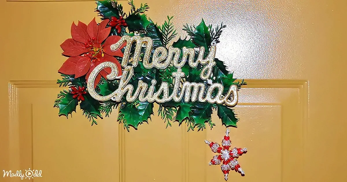 A festive Christmas wreath with "Merry Christmas" sign and red poinsettia on a yellow door.