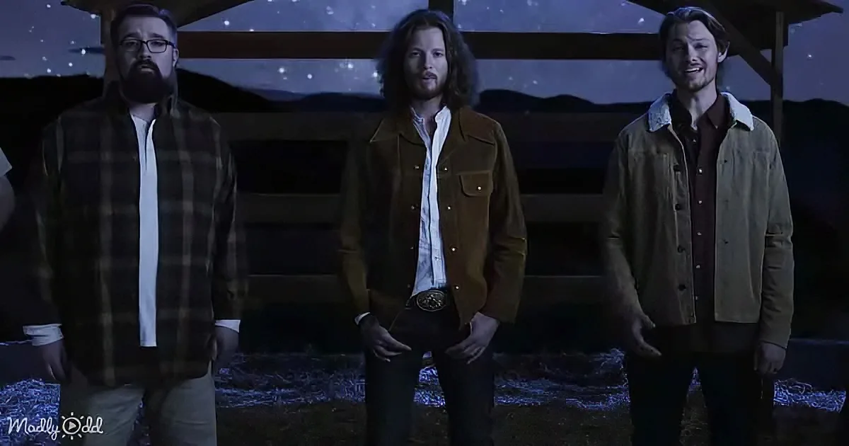Three men in casual attire stand in a dimly lit, starry night setting, possibly a desert.