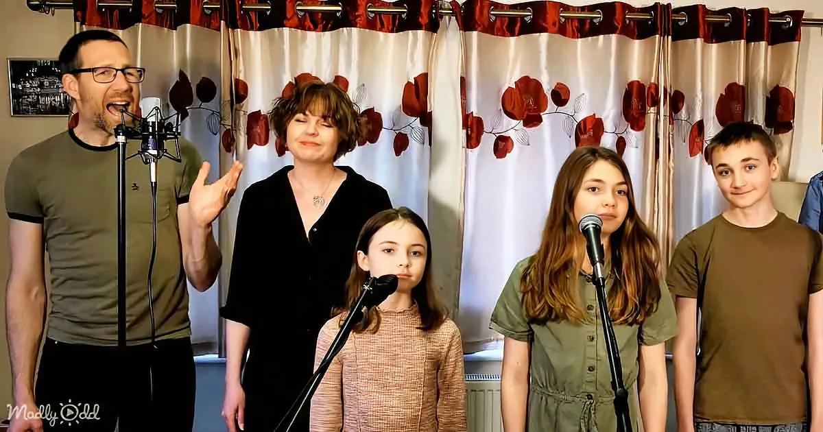 A family of five sings together in front of a floral curtain backdrop.