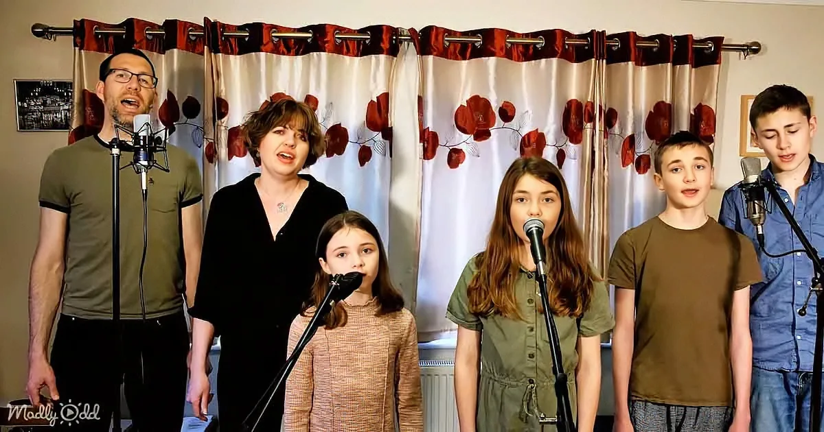 A family of six sings together in front of a floral curtain backdrop.