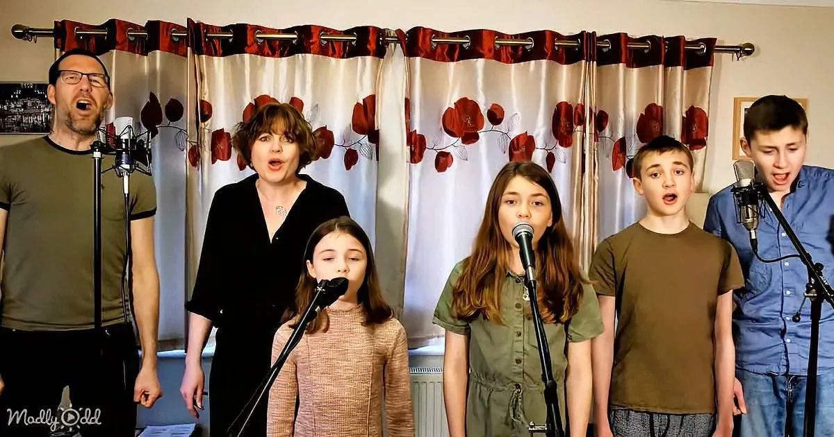 A family of six sings together in front of a floral curtain backdrop.