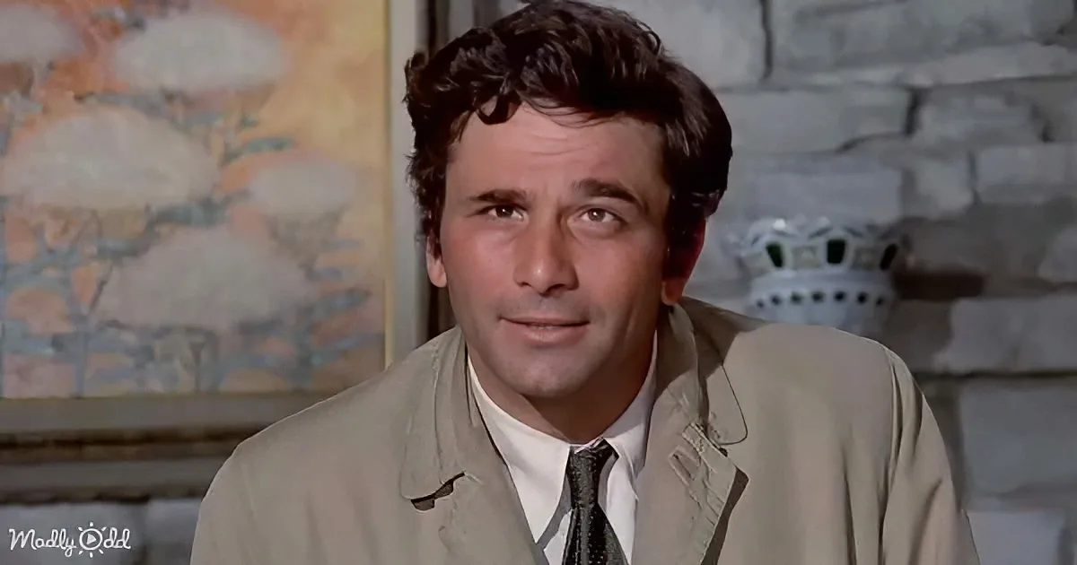 A man in a beige suit and tie smiles softly, with a brick wall and a painting in the background.