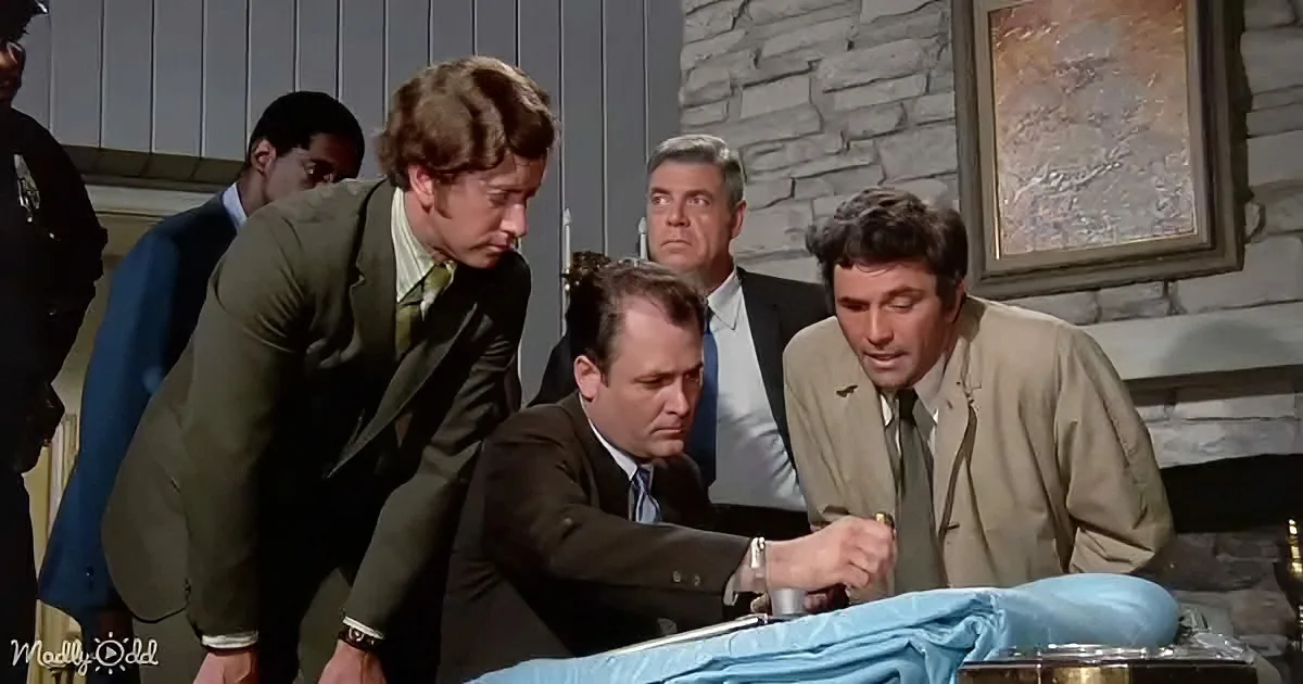 A man in a suit leans over a table, examining something with others observing closely.
