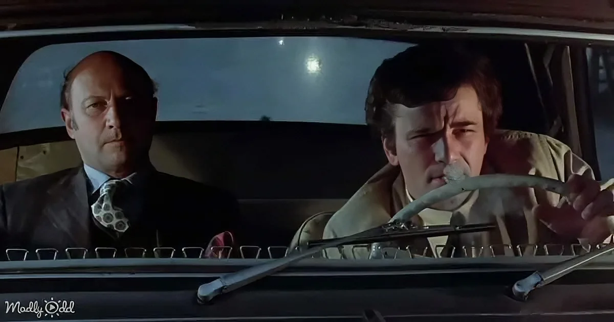 Two men in a car, one holding a snake, another looking concerned, night setting.