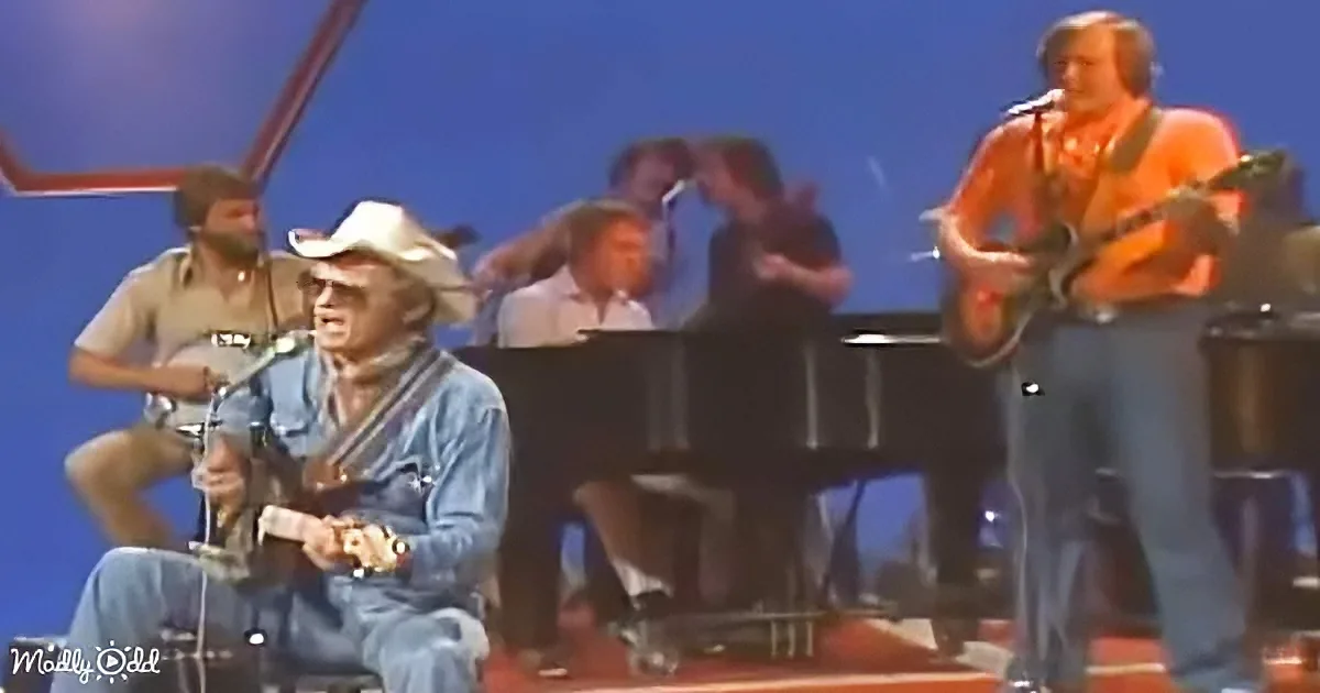 A man in a cowboy hat plays guitar while another man sings into a microphone on stage.