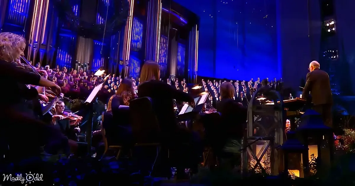 Conductor leads orchestra and choir in a grand performance under blue stage lighting.