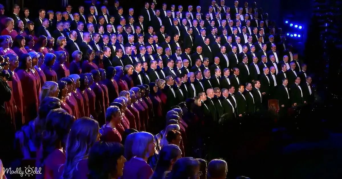 A large choir in formal attire stands in rows, illuminated by stage lighting.