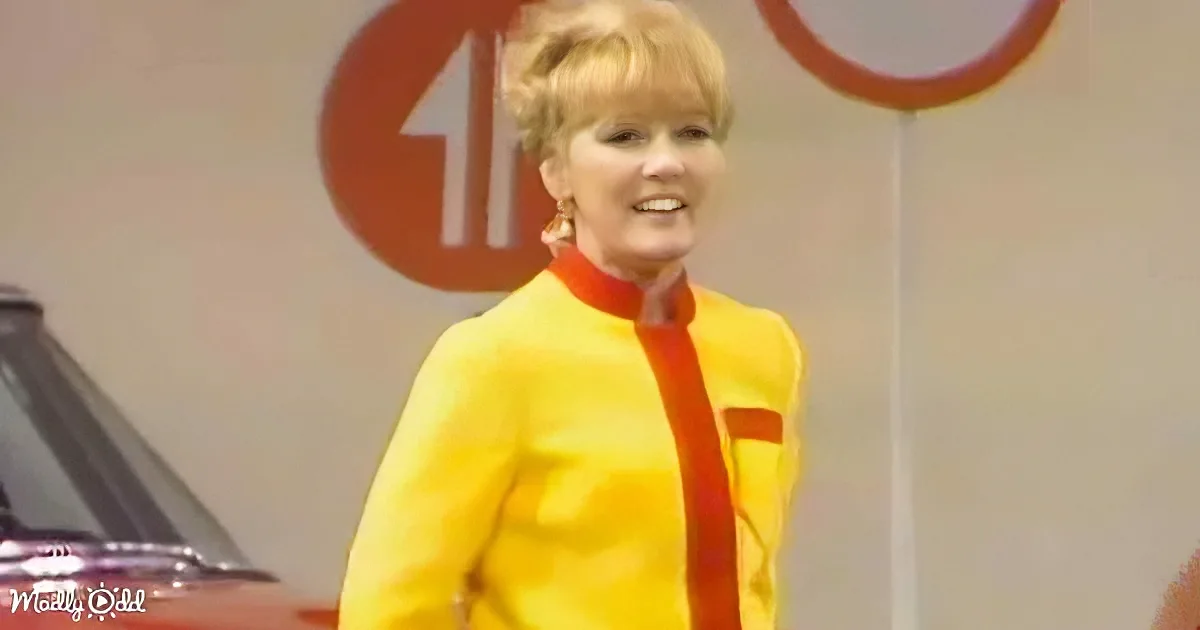 A woman in a yellow outfit smiles in front of a red sign with an arrow.