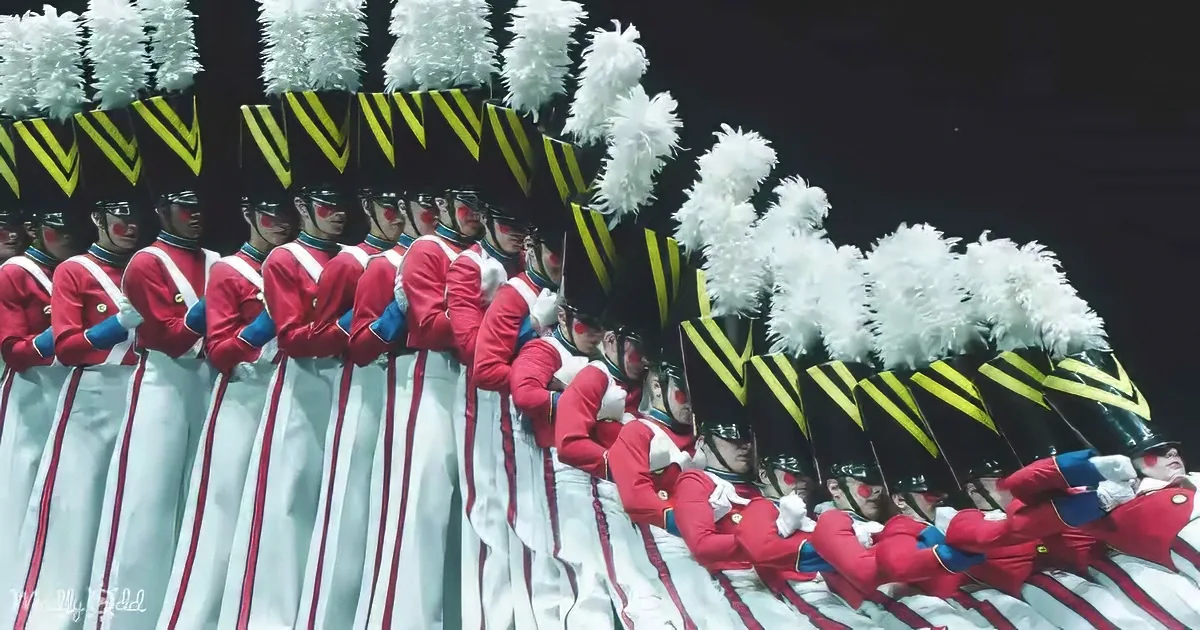 A group of uniformed performers in red and white costumes with black and yellow hats and white plumes.