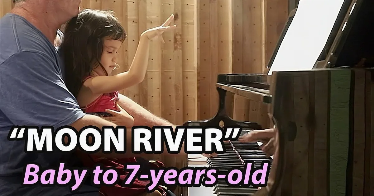 A man and a young girl play piano together in a wooden room.