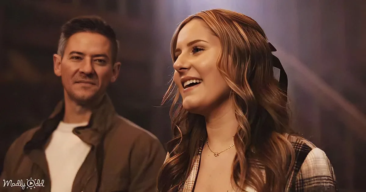 A woman with long brown hair smiles, wearing a plaid shirt and necklace, while a man in a brown jacket and white shirt...