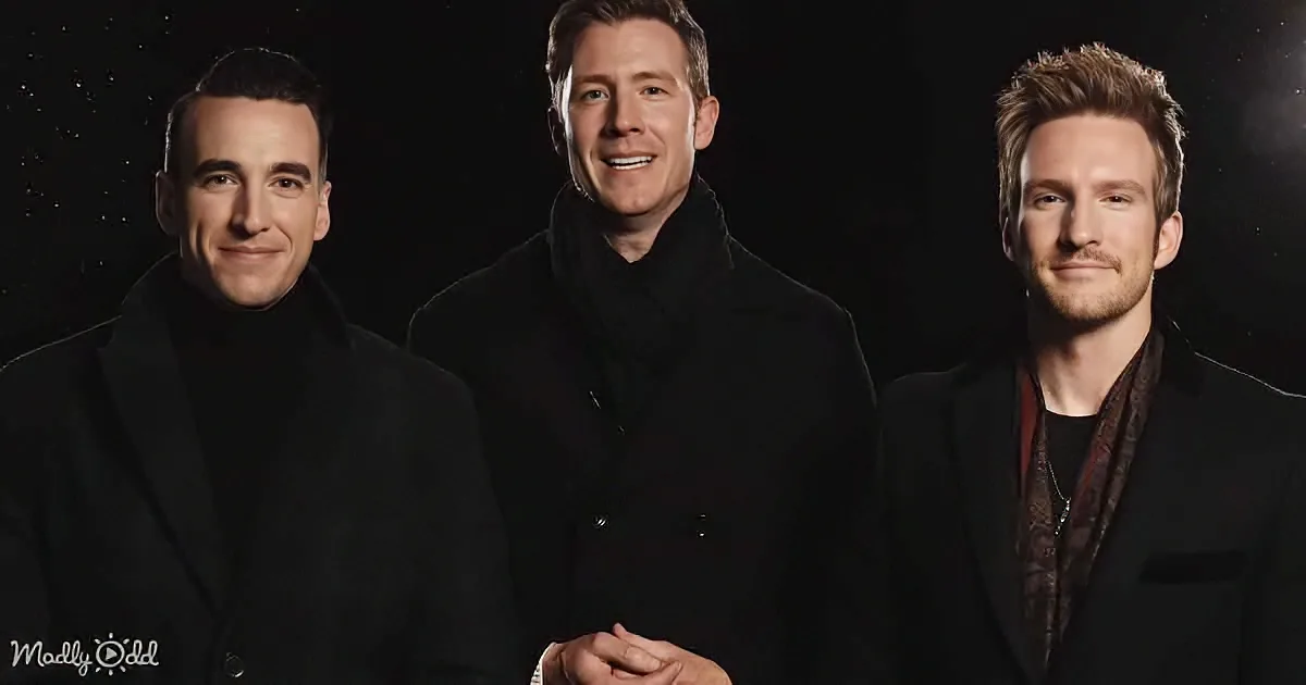 Three men in black attire stand together, smiling, against a dark background with faint star-like dots.