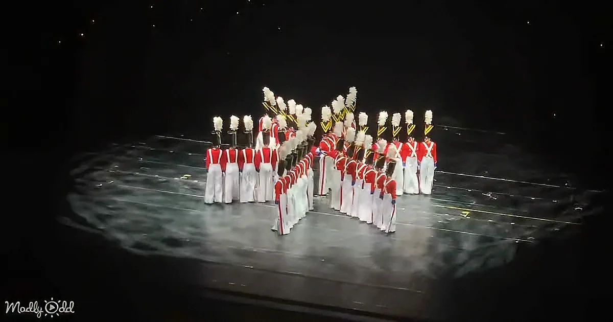 A marching band in red and white uniforms stands in formation on a stage.