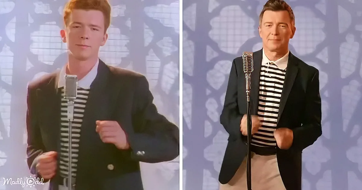 A man in a suit and striped shirt stands with a microphone, holding it in front of a patterned background.