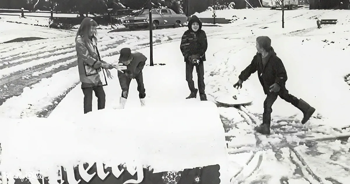 Children play in snow, building a large snowman with a "Merry" sign in the foreground.