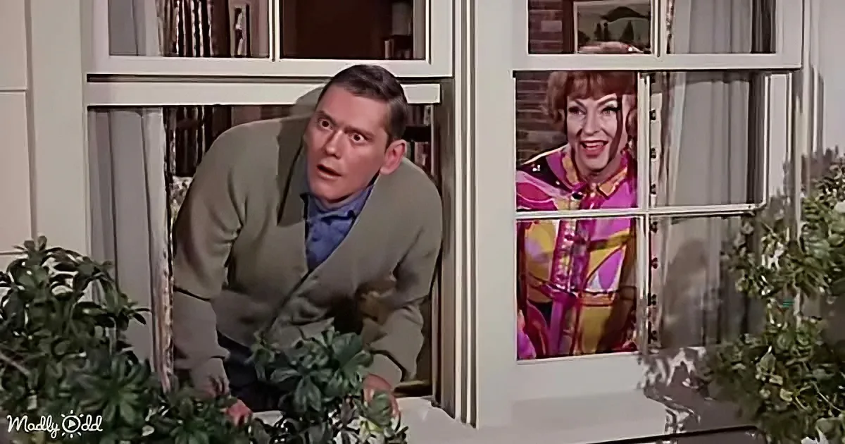 A man leans over a table, looking surprised, while a woman in a colorful dress peers out of a window.