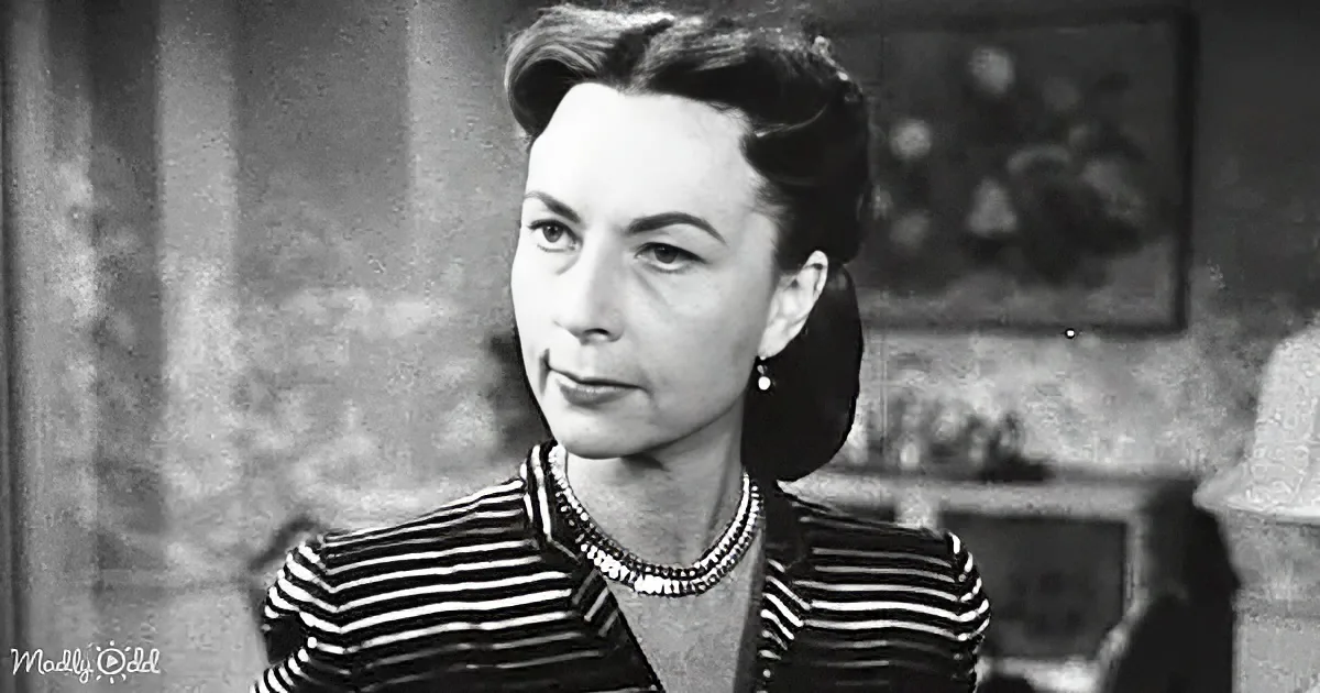 A woman in a striped shirt and pearl necklace, looking to the side, with a blurred background.