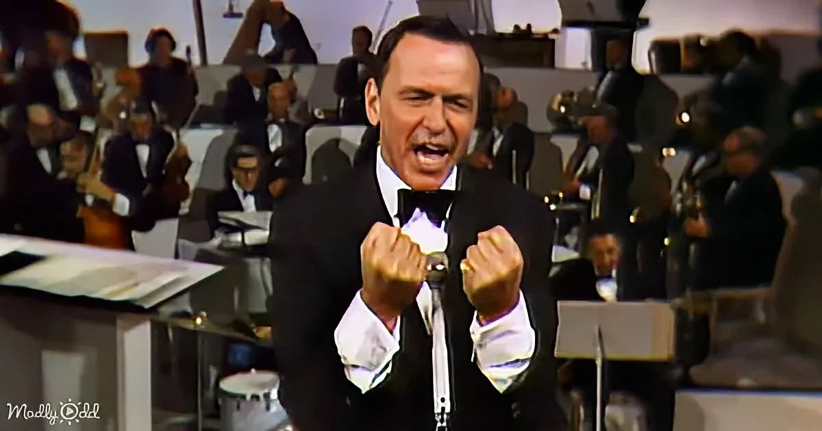 Frank Sinatra in a tuxedo, holding a microphone, with an orchestra in the background.