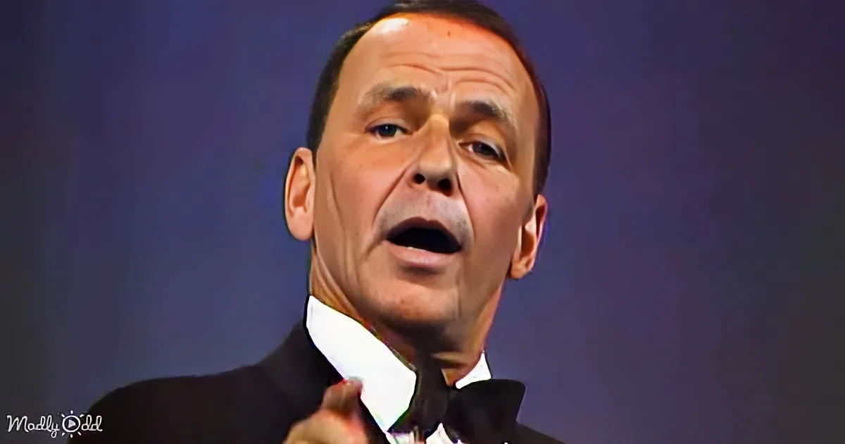A man in a tuxedo is singing passionately, with his hand raised, against a dark background.