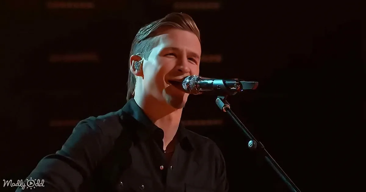 A person in a black shirt sings into a microphone on stage.