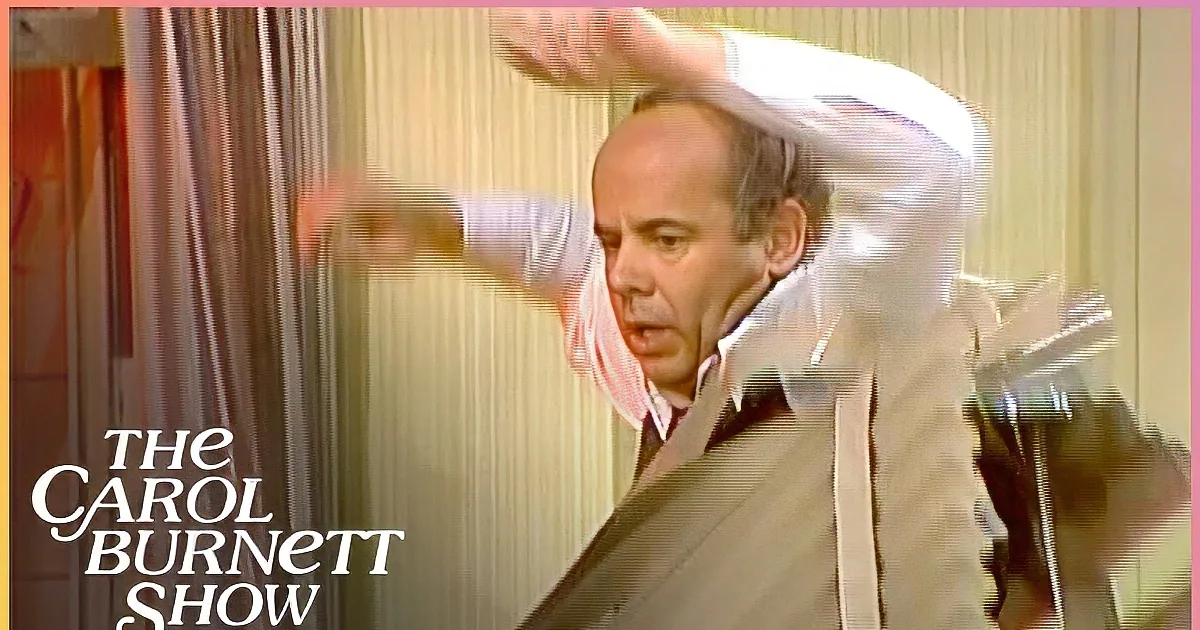 A man in a vest and tie adjusts his hair and then leans against a wall, appearing to be in a dressing room.