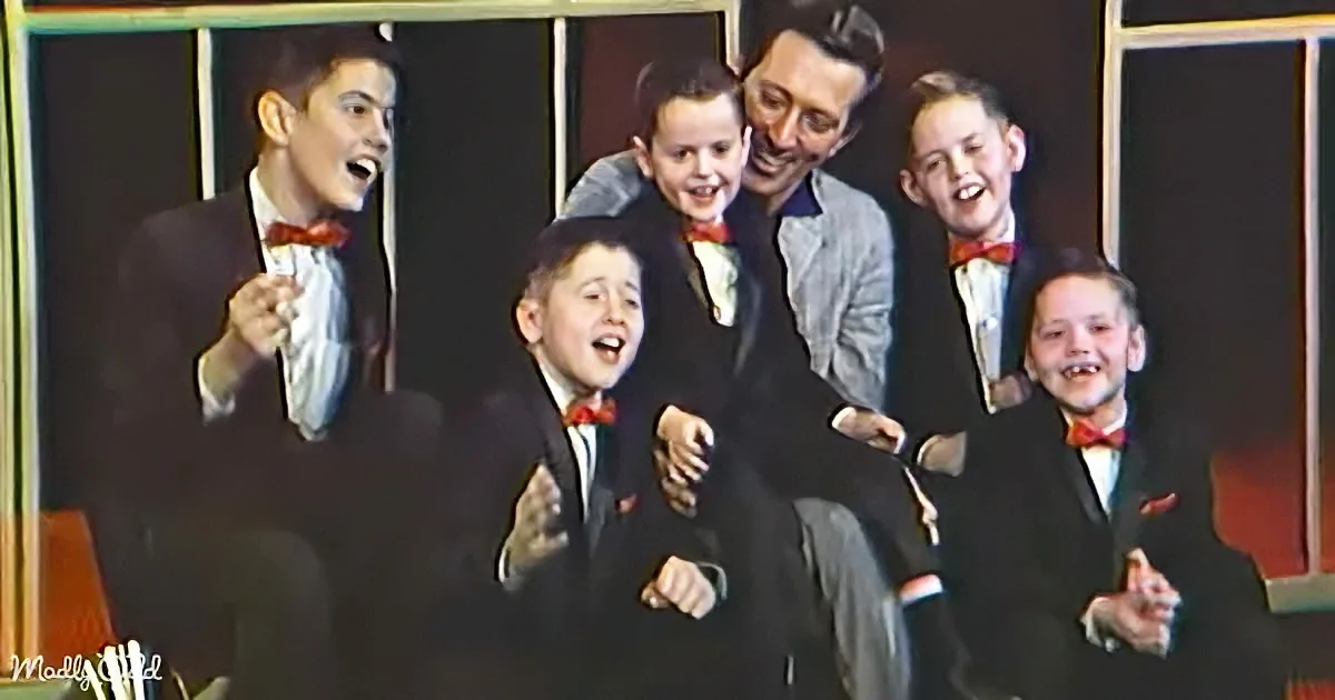 A man in a suit and bow tie is surrounded by five young boys in suits and bow ties, all smiling and laughing.