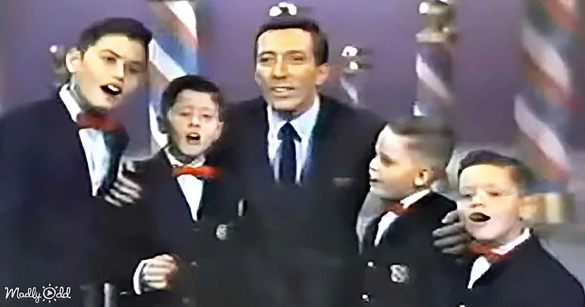A man in a suit sings with four young boys in suits and bow ties, all appearing to perform.