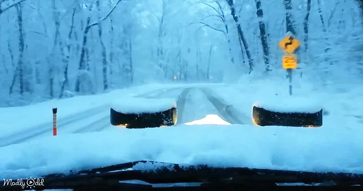 Snow-covered road with a yellow road sign and snow-laden car windshield.