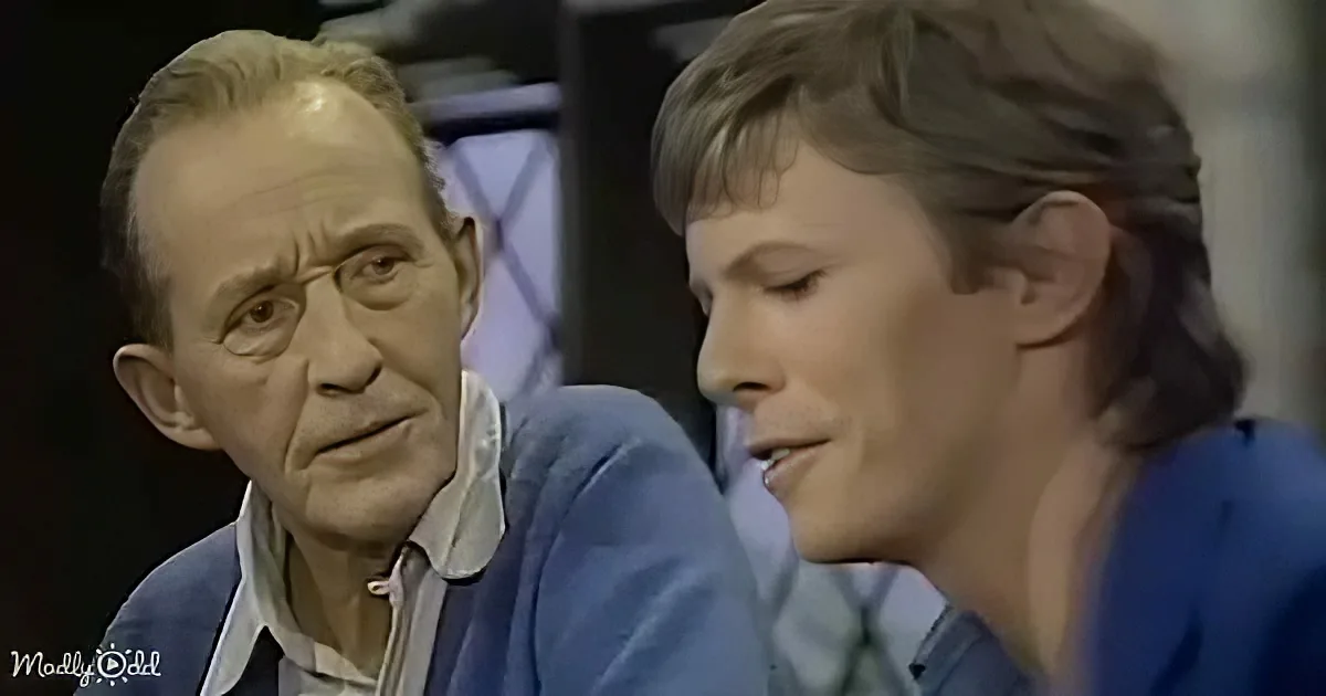 An older man in a blue shirt is speaking to a younger man in a similar outfit, both seated and engaged in conversation.