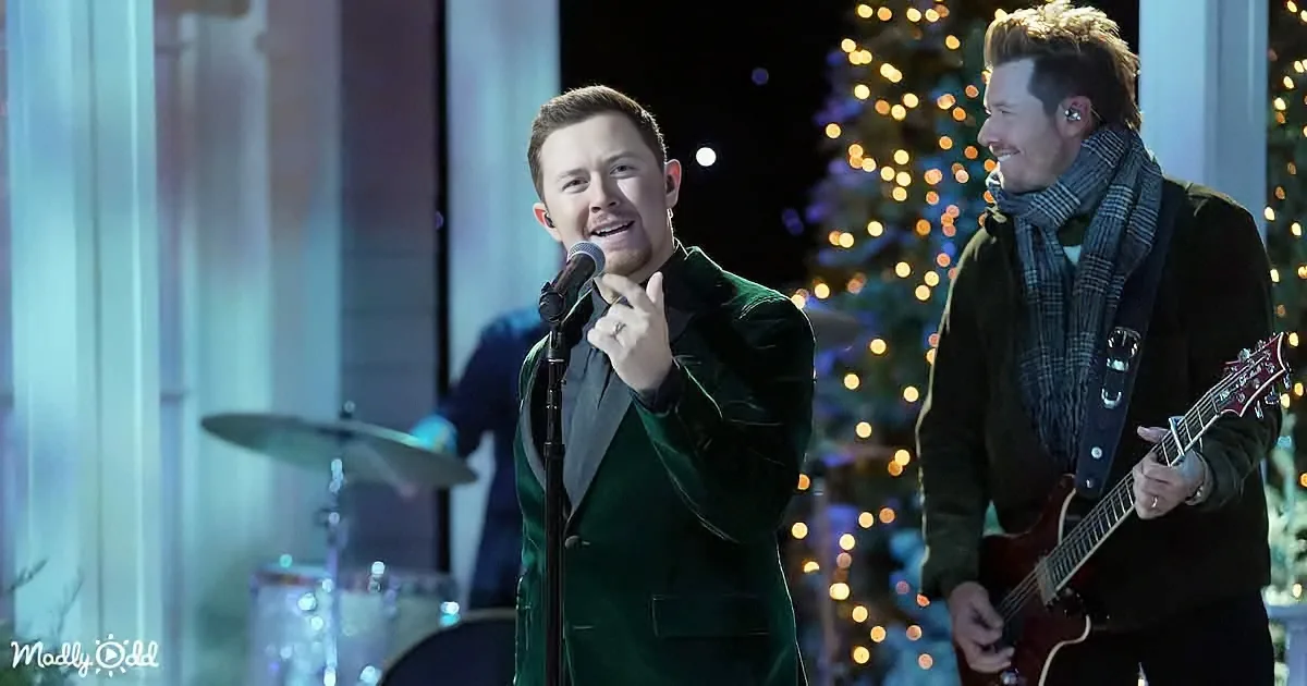A man in a green suit sings into a microphone, smiling, with another man playing guitar beside him.
