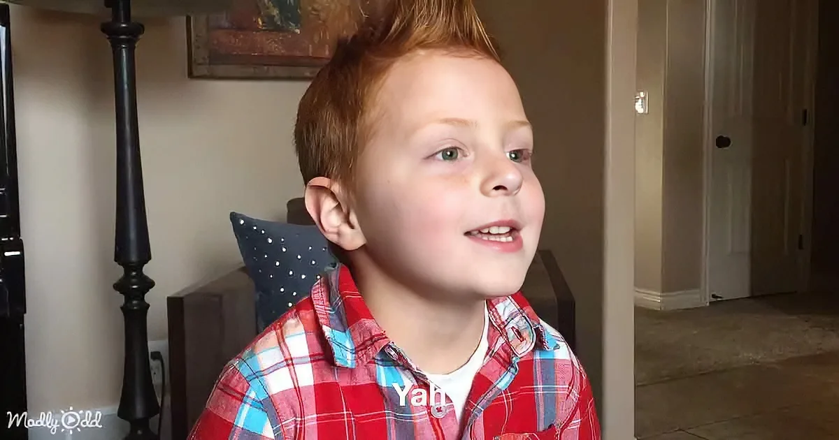 A young boy with red hair and a plaid shirt smiles, looking to the side, with a pillow behind his head.