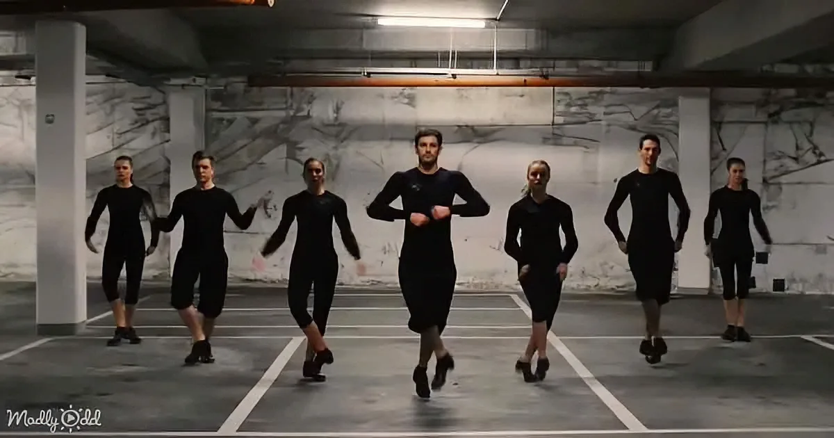 A group of dancers in black outfits perform a synchronized routine in a dimly lit parking garage.