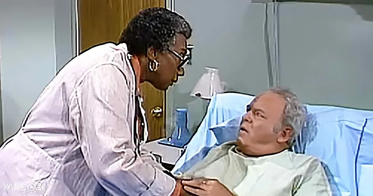 A doctor in a white coat leans over a patient in a hospital bed, engaging in conversation.