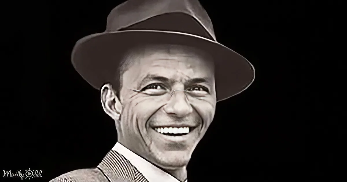 A smiling man wearing a fedora and suit jacket, against a dark background.