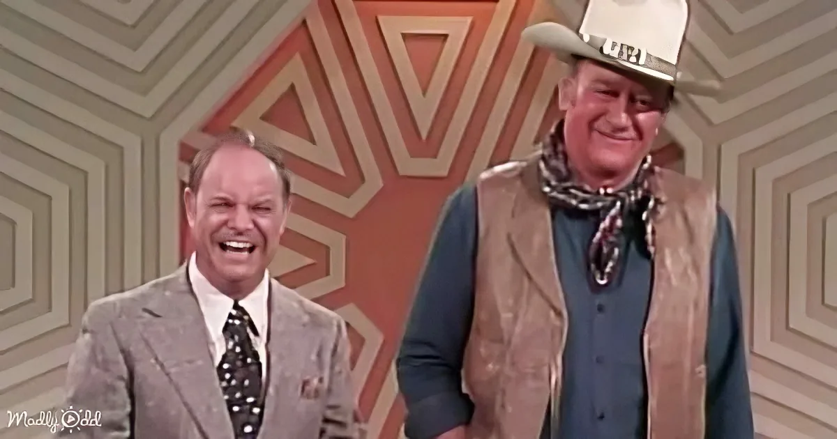 A man in a cowboy outfit and another in a suit are smiling in front of a geometric-patterned background.