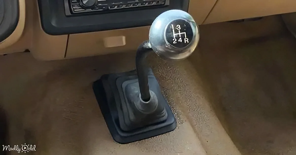 A manual gear shift with a silver knob and black numbers is in a car's interior.