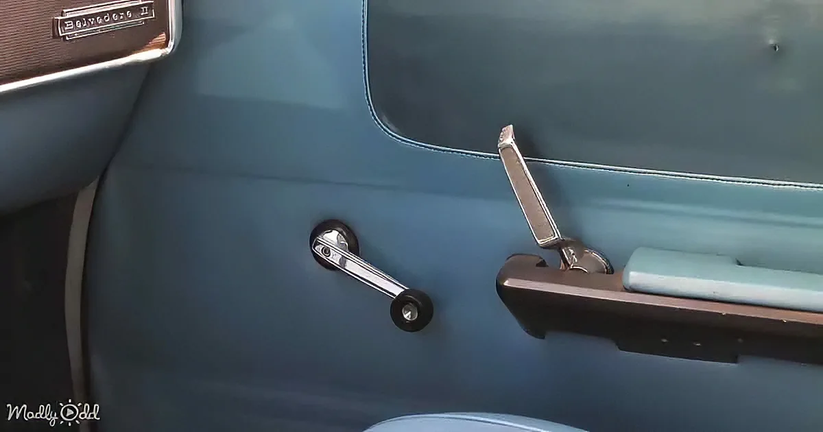 A vintage car door with a chrome handle and window crank, featuring a teal interior.
