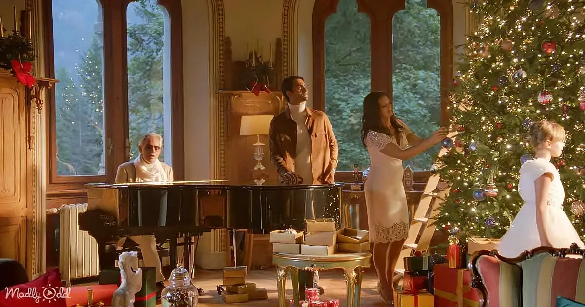 A man in white plays piano as others decorate a Christmas tree in a festive living room.