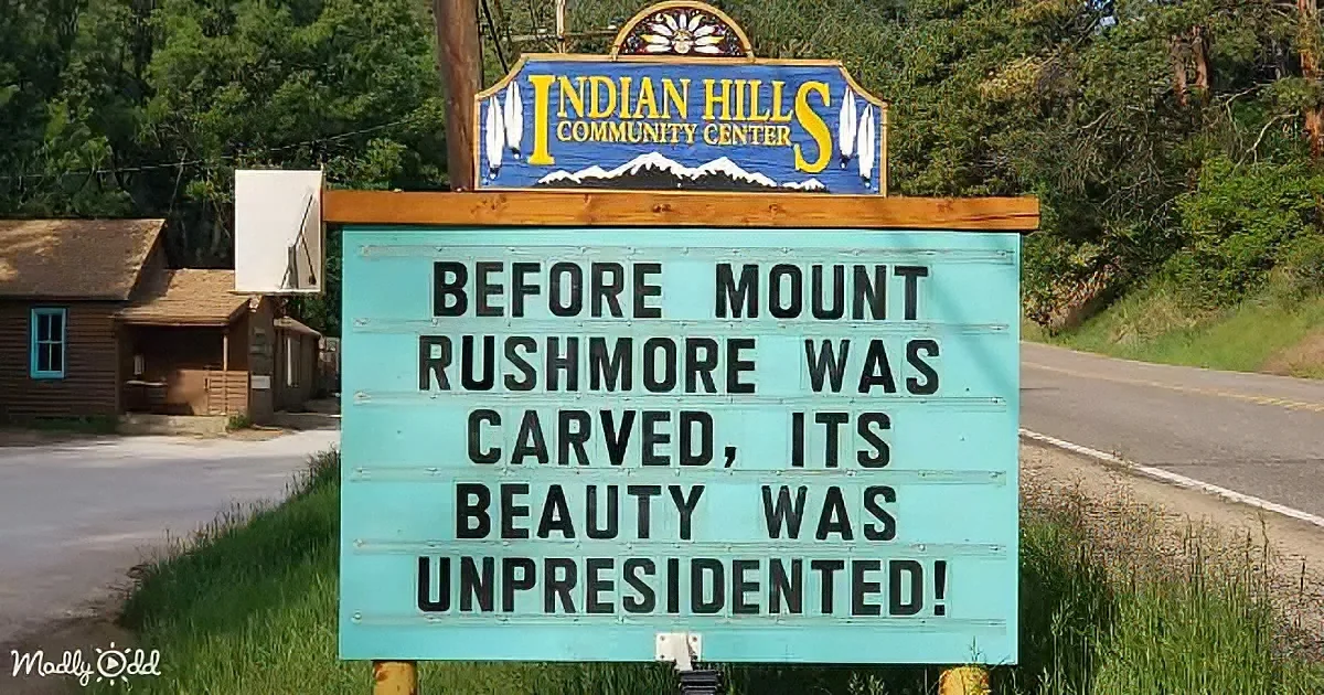 A sign at Indian Hills Community Center humorously notes Mount Rushmore's natural beauty before carving.